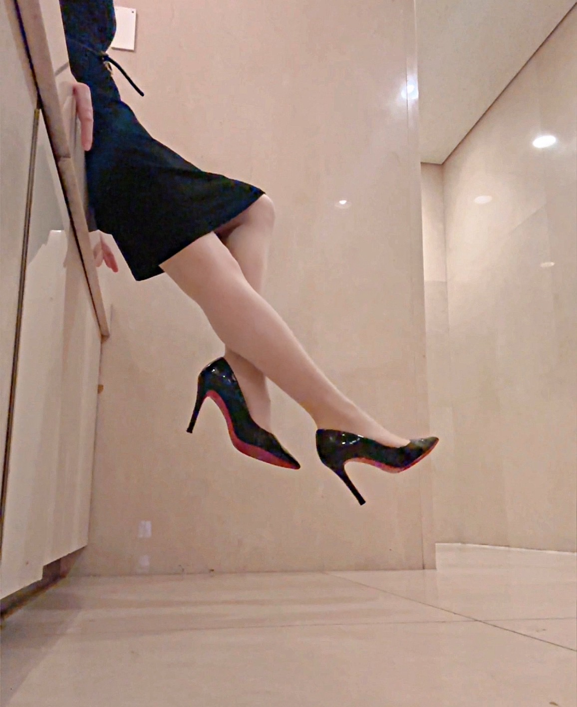 黒いタイトスカートに赤いピンヒールを履いた女性が壁際で脚を伸ばす姿。ピンヒールフェチや脚フェチ向けの魅力的なシルエット。